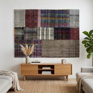 Könnte beinhalten: Ein großer rechteckiger Wandteppich mit einem Patchwork-Design aus verschiedenen gewebten Stoffbahnen in den Farben Dunkelrot, Blau, Grau und Braun. Das Textil zeigt eine Mischung aus karierten, gestreiften und einfarbigen Mustern mit sichtbaren Nähten.