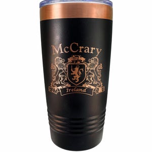 May include: Black insulated tumbler with a copper-colored rim and lid. The tumbler features the name "McCrary" and a family crest with the word "Ireland" in a copper color.