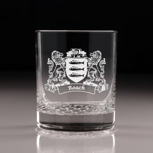 May include: A clear, etched glass tumbler featuring a family crest design. The crest includes a shield with three fish, a banner with the name "Roach", and is flanked by two lions. The glass has a textured base.