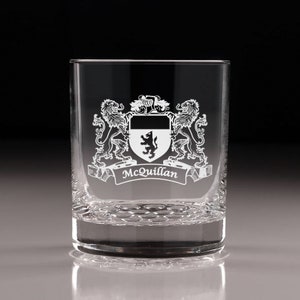 May include: A clear glass tumbler with a detailed family crest etched on the front. The crest features a shield with a lion, flanked by two lions, and the name "McQuillan" on a banner below. The glass has a textured base.
