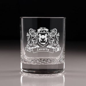 May include: A clear, engraved rocks glass featuring a family crest design. The crest includes two lions, a shield, and the name "Laverty" on a banner. The glass has a textured base and is suitable for whiskey or other beverages.