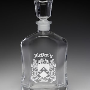 May include: A clear glass decanter with a square base and a stopper. The decanter features the name "McDevitt" and a family crest with the word "Ireland" below it. The stopper is rectangular.