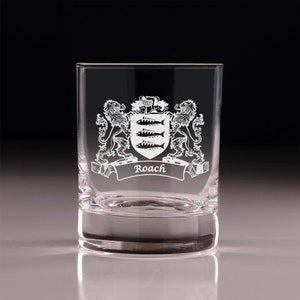 May include: A clear, square-shaped rocks glass with an etched family crest design. The crest features a shield with three fish, flanked by lions, and the name "Roach" on a banner. The glass is suitable for whiskey or other beverages.