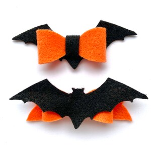 May include: Two felt Halloween hair bows. One bow is black with orange felt wings and the other is orange with black felt wings.