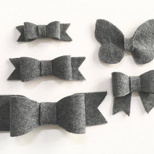 May include: Five gray felt bows of varying sizes. The largest bow is a butterfly shape. The bows are perfect for adding a touch of whimsy to crafts, gifts, or home decor.