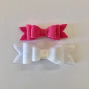 Könnte beinhalten: Zwei Filzbänder, eines rosa und eines weiß. Die Schleifen liegen übereinander.