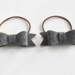 May include: Two gray felt hair bows with brown elastic bands.