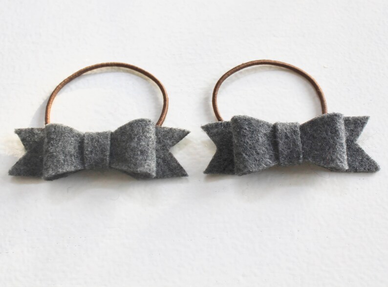 May include: Two gray felt hair bows with brown elastic bands.