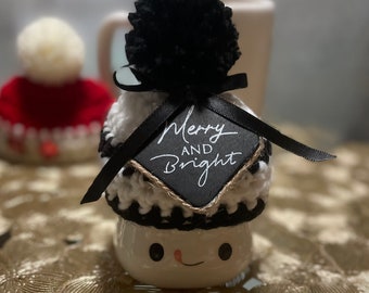 Puede incluir: Taza de cerámica blanca con forma de muñeco de nieve con un gorro de punto negro y blanco con un pompón negro. El gorro tiene una cinta negra con un letrero de pizarra negra que dice "Merry and Bright".