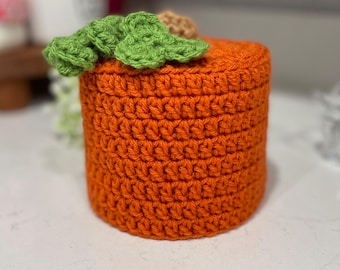 Puede incluir: Cubierta de rollo de papel higiénico de ganchillo naranja con hojas de ganchillo verdes en la parte superior.