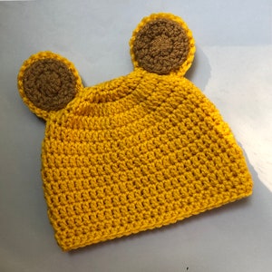 May include: A yellow crocheted hat with brown crocheted ears. The hat is made with a single crochet stitch.
