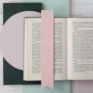 May include: A close-up of an open book with a pink bookmark that says "SARAH" on it. The book is open to a page with text about a printing hall that is being renovated. The text mentions the Factory Act of 1901.