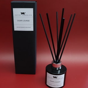 May include: Black and white label on a black glass bottle with a silver lid and black reeds. The label reads "Catsy Candles Cigar Lounge Hand Made Fragrance Oil Reed Diffuser".