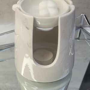Pode incluir: Aquecedor de cera branco de cer&acirc;mica com design de m&aacute;rmore. O aquecedor tem um prato superior para derreter cera e um compartimento inferior para uma vela de ch&aacute;.