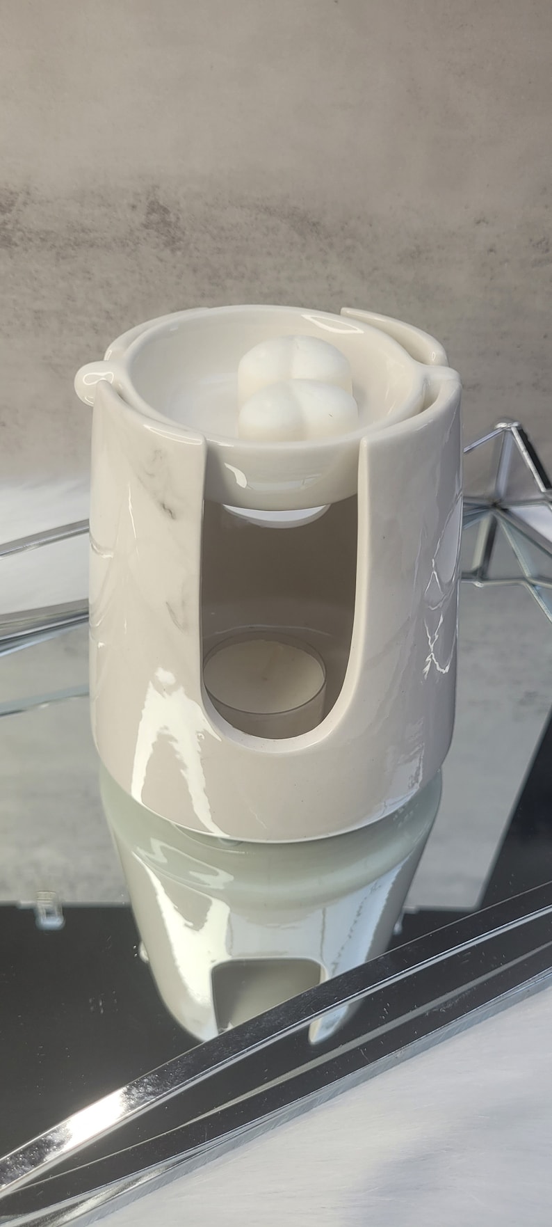 Pode incluir: Aquecedor de cera branco de cer&acirc;mica com design de m&aacute;rmore. O aquecedor tem um prato superior para derreter cera e um compartimento inferior para uma vela de ch&aacute;.