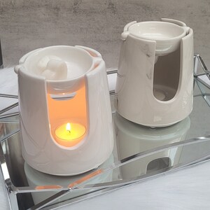 Pode incluir: Dois aquecedores de cera de cer&acirc;mica branca com uma vela de ch&aacute; em um dos aquecedores. Os aquecedores est&atilde;o em uma bandeja de espelho prateada.