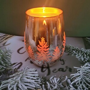 May include: A glass candle holder with a gold finish and a design of orange trees. The candle is lit and the wax is melted.