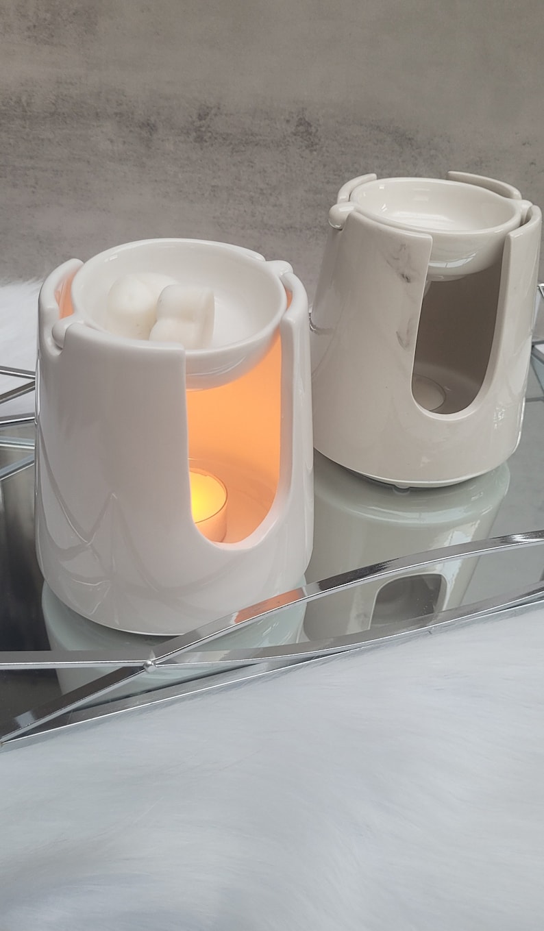 Pode incluir: Dois aquecedores de cera de cer&acirc;mica branca com um design de m&aacute;rmore. O aquecedor &agrave; esquerda tem uma vela de ch&aacute; acesa e duas ceras derretidas na tigela superior. O aquecedor &agrave; direita tem um design branco liso.