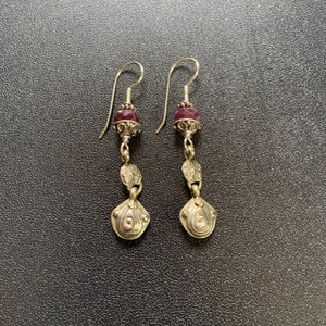 May include: A pair of silver dangle earrings with a purple gemstone bead and a floral design.