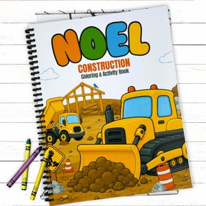 A personalized childrens full color construction coloring book cover featuring the name NOEL flatlay on a white wood background with scattered loose wax crayons.