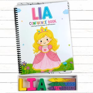 May include: A spiral-bound coloring and activity book titled LIA CONFIDENCE BOOK with a cartoon princess illustration on the cover. Below the book is a white box containing the letters L, I, A in yellow, pink, and green, and three crayons.