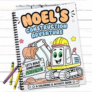 A personalized black and white construction book cover for NOEL neatly filled in with colored pencils on a white wood surface with crayons in the corner.