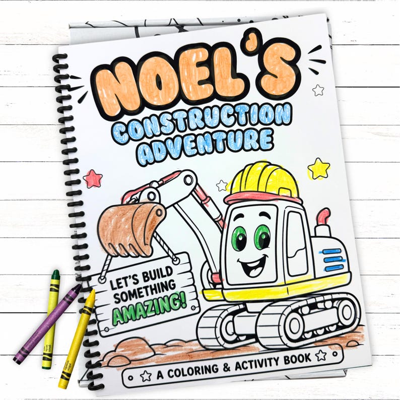 A personalized black and white construction book cover for NOEL neatly filled in with colored pencils on a white wood surface with crayons in the corner.