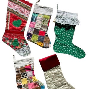 May include: Five assorted Christmas stockings. One red stocking with a green heart and lace trim. Another is patchwork with various fabric patterns. A green stocking with a white lace trim. Two more patchwork stockings and a quilted cream stocking with a red cuff.