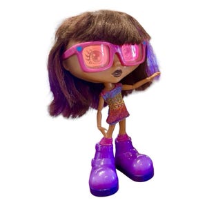 May include: A doll with brown hair, purple highlights, and pink-framed sunglasses. The doll wears a colorful dress and large purple boots. The doll's arms are outstretched, and it has a dark complexion.