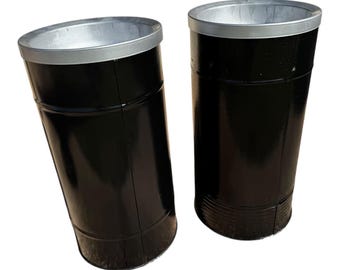 May include: Two black metal containers with a shiny finish and silver rims. The cylindrical containers have a slightly tapered shape and are set against a white background. The containers appear to be empty.