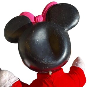 May include: A Minnie Mouse plush toy, featuring large black ears and a pink bow. The toy is wearing a red outfit with white gloves. The Disney logo is visible on the toy.