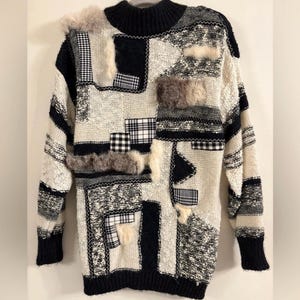 May include: A patchwork sweater in a mix of black, white, and gray. The sweater features various textures, including knit, plaid, and faux fur accents. The design includes a high, ribbed collar and cuffs.