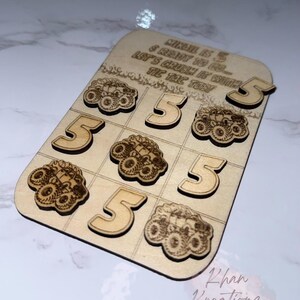 May include: Wooden tic-tac-toe game with laser-cut monster truck and number 5 designs. The game board has the text "MIKAEL IS 5 & READY TO GO... LET'S CRUSH IT WITH TIC TAC TON". Includes 9 game pieces.