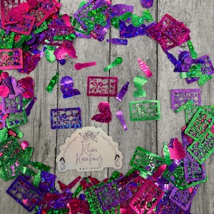 May include: A collection of colorful, glittery craft supplies, including cut-out shapes and stencils. The shapes include bottles, microphones, and text that reads "Demon Hunters". The colors are pink, green, purple, and blue.