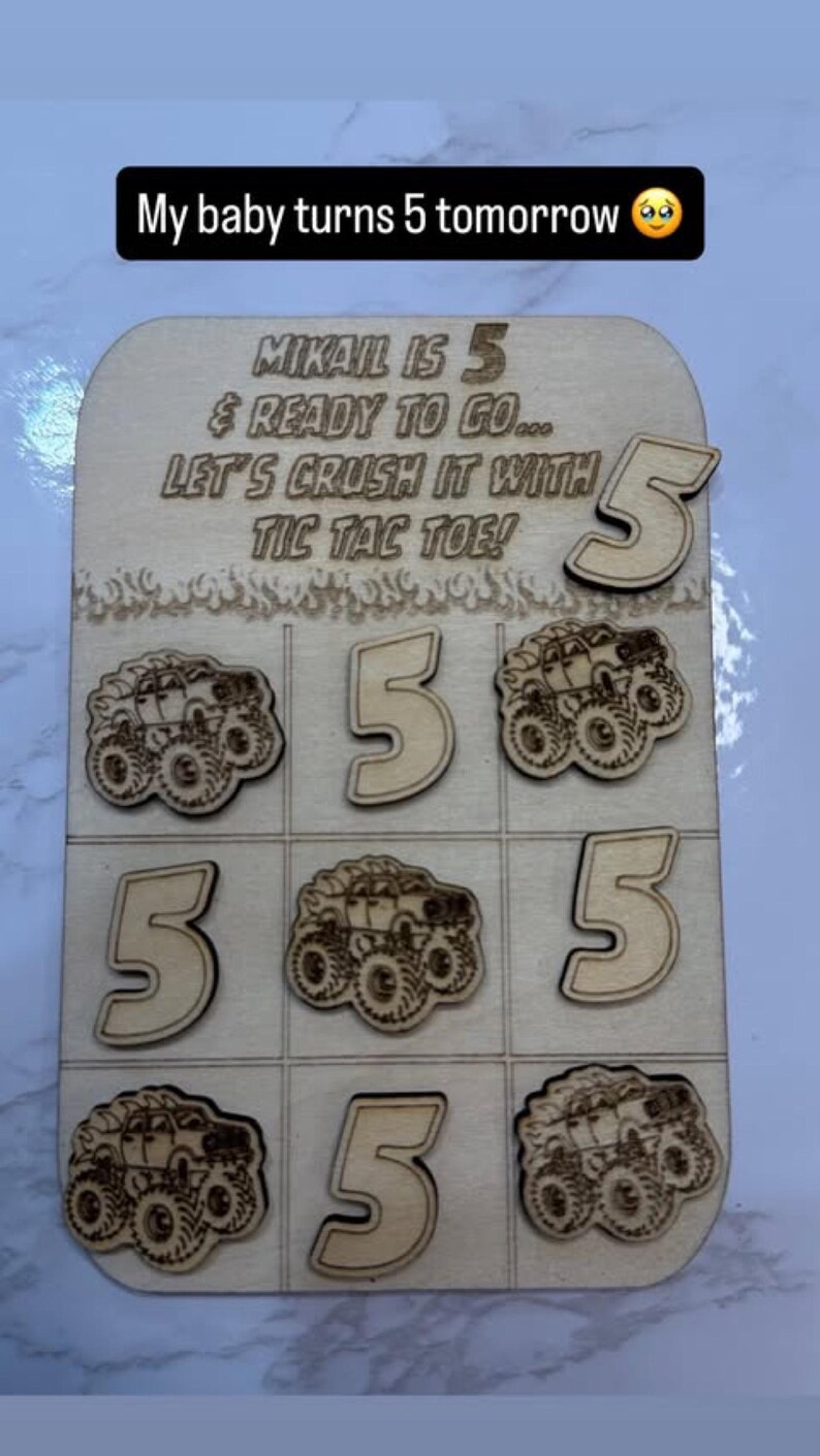 May include: Wooden tic-tac-toe game with the text "My baby turns 5 tomorrow". The game board features the number 5 and monster truck designs. The text "MIKAIL IS 5 & READY TO GO... LET'S CRUSH IT WITH TIC TAC TOE!" is also present.