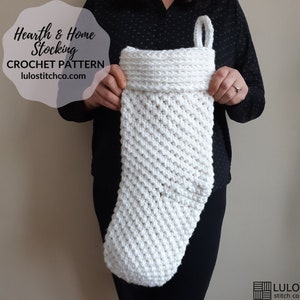 May include: A white crochet Christmas stocking with a folded cuff and a loop for hanging. The text "Hearth & Home Stocking CROCHET PATTERN lulostitchco.com" is visible on the upper left. The stocking is held by a person.