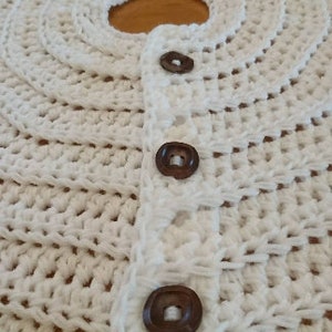 Puede incluir: Falda de &aacute;rbol de crochet blanco con botones marrones. La falda tiene un borde festoneado y est&aacute; hecha con un punto de crochet simple.