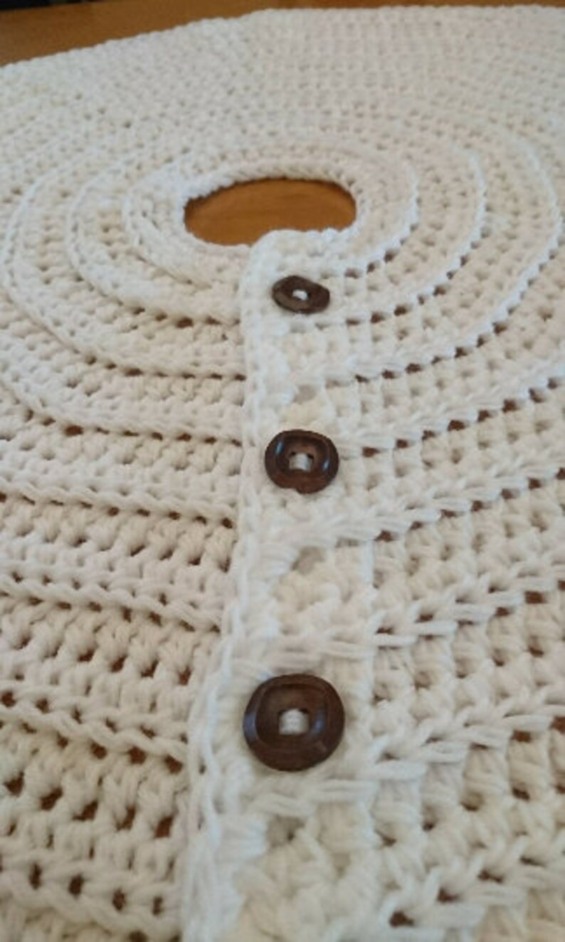 Puede incluir: Falda de &aacute;rbol de crochet blanco con botones marrones. La falda tiene un borde festoneado y est&aacute; hecha con un punto de crochet simple.