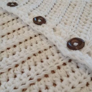 Puede incluir: Falda de &aacute;rbol de crochet blanco con botones marrones. La falda est&aacute; hecha de un delicado patr&oacute;n de punto abierto.