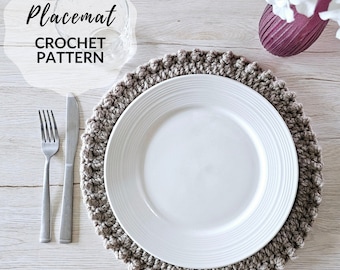 May include: A crocheted placemat in a light brown color with a white plate on top. The placemat has a textured, bumpy surface. The text "Placemat CROCHET PATTERN" is visible in the top left corner of the image.