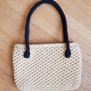 May include: A beige crocheted tote bag with black crocheted handles.