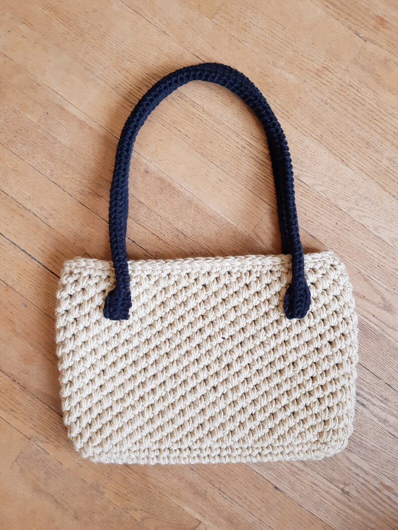 May include: A beige crocheted tote bag with black crocheted handles.