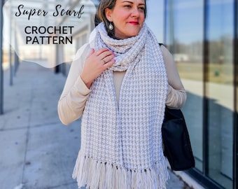 May include: A white and beige crochet scarf with fringe. The scarf is worn by a person standing in front of a building. The text "Super Scarf CROCHET PATTERN" is visible in the image.
