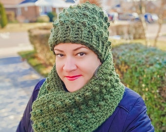 May include: A green crocheted hat and scarf set with a fuzzy pom pom on the hat. The hat and scarf are made with a textured stitch.