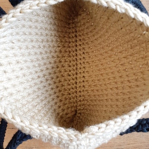 May include: A beige crocheted tote bag with black rope handles. The bag is open and the inside is visible.