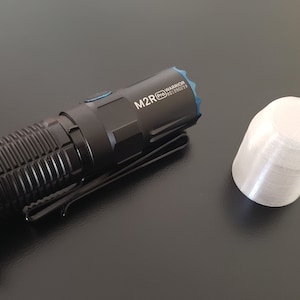 May include: A black flashlight with a blue accent and the text "M2R PRO WARRIOR SST40" on the side. A white metal cap is also shown.