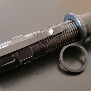May include: A black flashlight with a blue ring around the end and a black pocket clip. The flashlight has a textured body and the brand name "OLIGHT" is printed on the side.