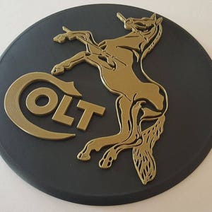 May include: A black circular plaque with a gold-coloured Colt logo and a stylised horse design. The logo reads "COLT" in all caps.