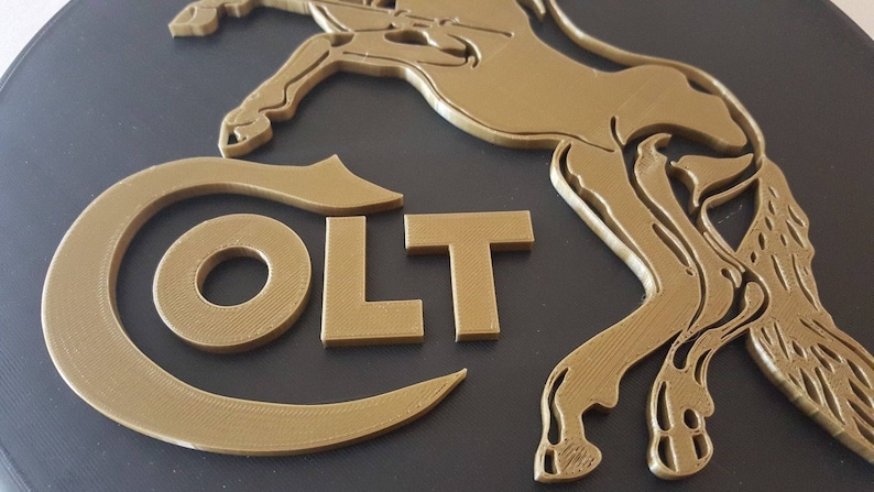 May include: A gold-coloured metal plaque with a stylised horse and the word "COLT" in raised letters.
