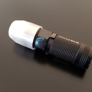 May include: A black flashlight with a white diffuser on the end. The flashlight has a textured body and a blue button.
